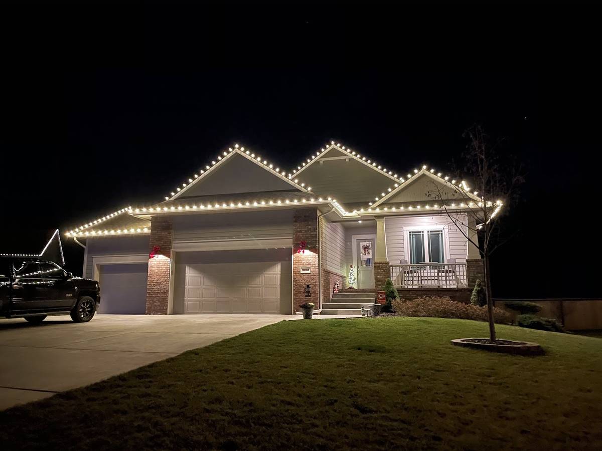 A one-story brick and siding house at night with a string of white lights outlining the roofline and garage.