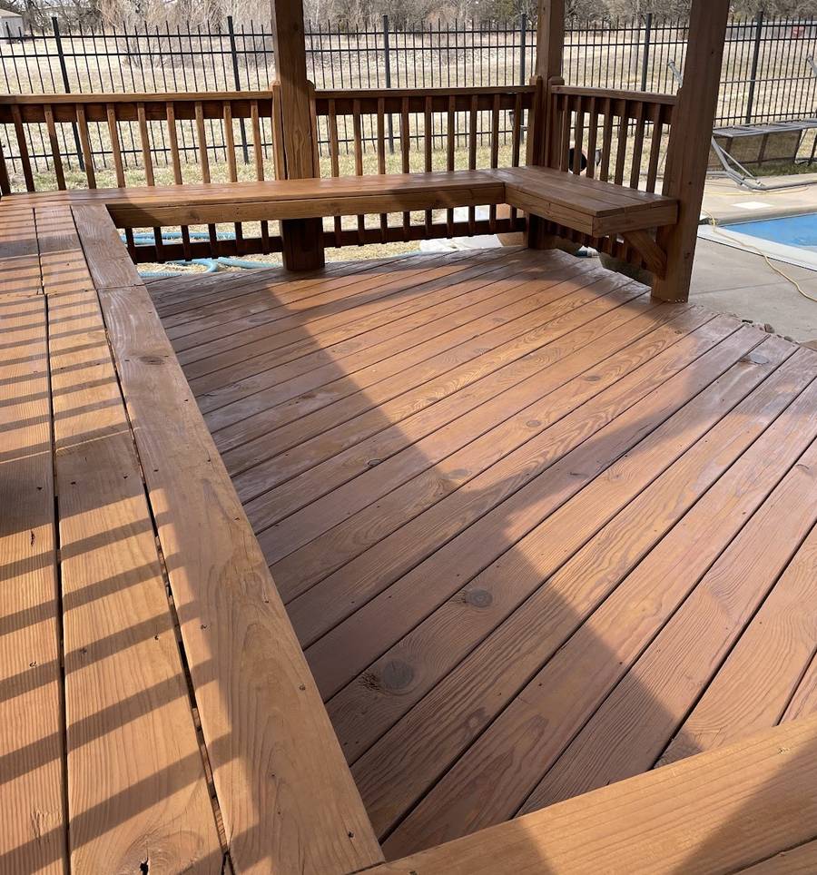 A newly stained wood deck with a built-in corner bench and railing, and a pool cover visible beyond the rail.